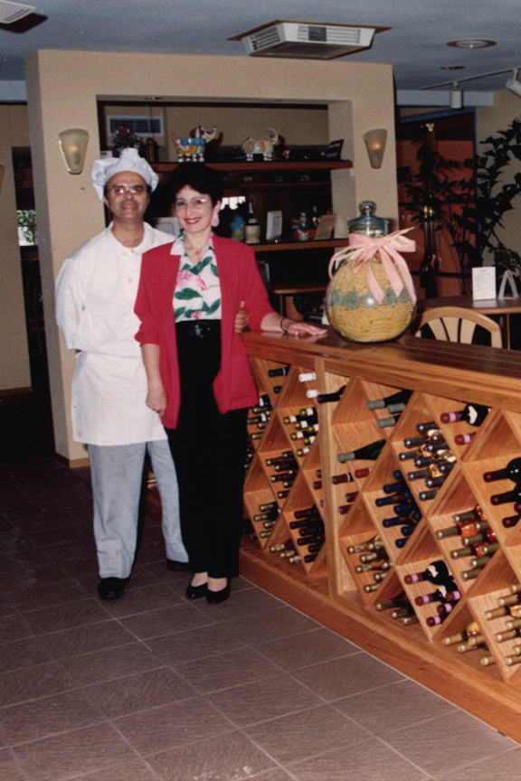 John and Gail stand in front of the beautiful wine rack inside their Whittier restaurant.